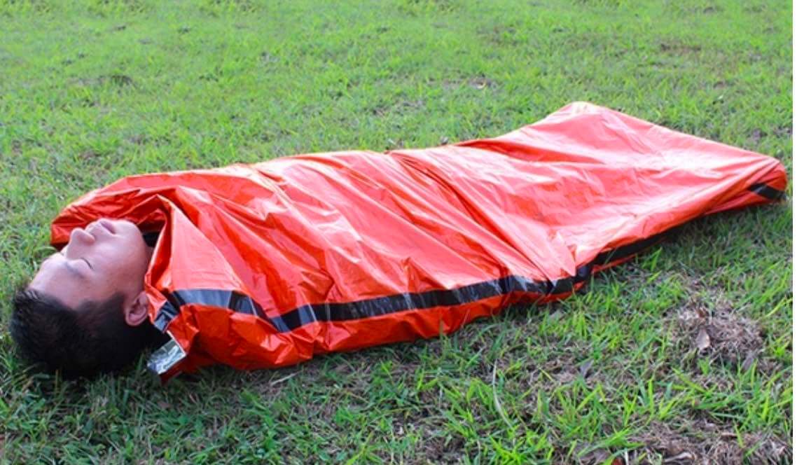 a man laying on the ground wearing the emergency sleeping bag